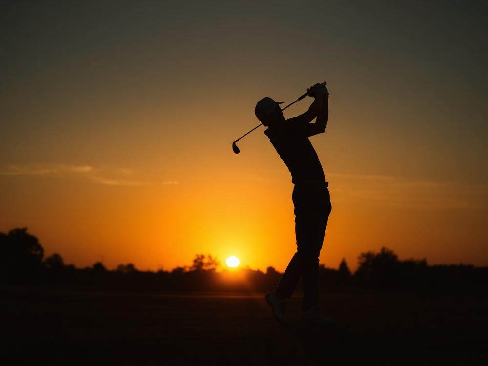 Golfer silhouetted at sunset on a course